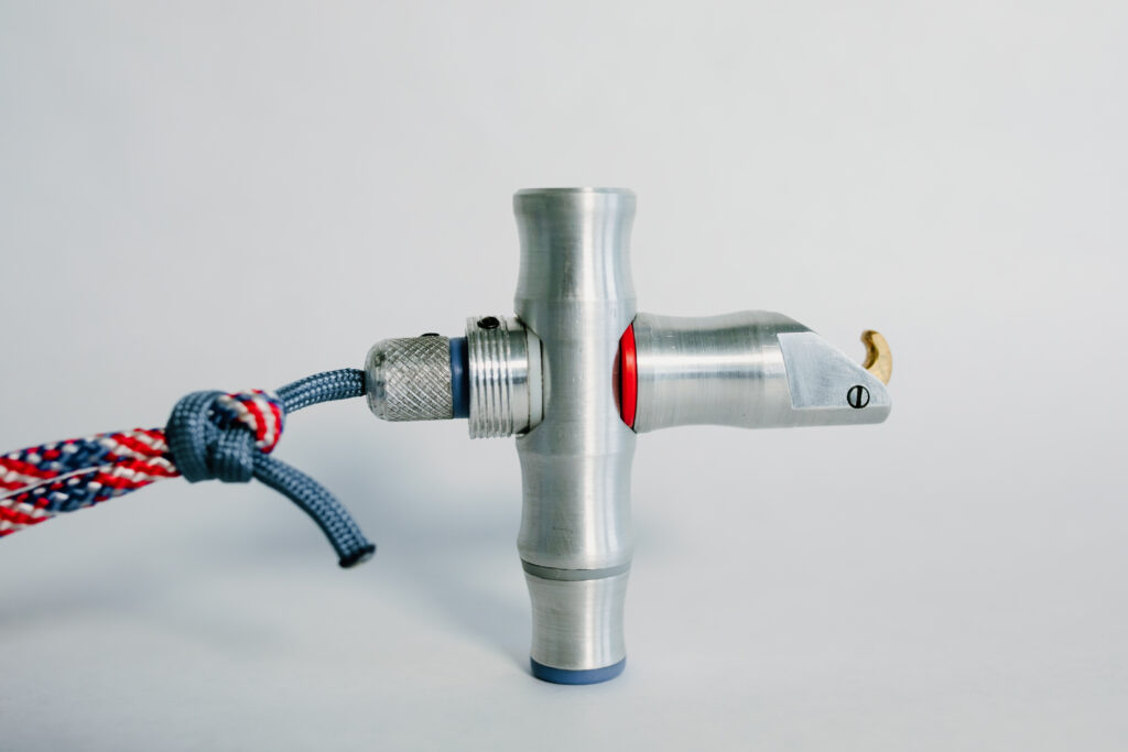 A silver metal skydiving cutaway handle with a blue and red cord attached, photographed against a light gray background.